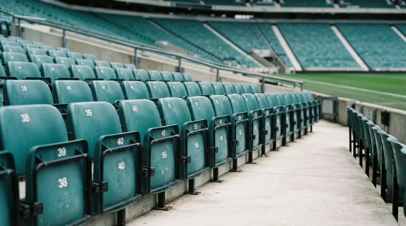 Rząd pustych plastikowych krzesełek na trybunie stadionu w świetle dnia.